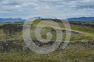 Unrecognisable people on the coastline around the pond Stakholstjorn with pseudo craters - natural monument near Lake Myvatn in