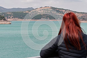 unrecognisable red-haired woman observes reservoir with turquoise water