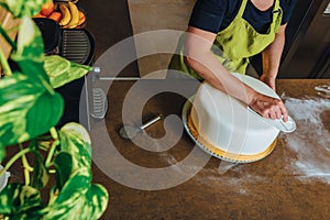 Unrecognisable woman in bakery decorating wedding cake with white fondant.