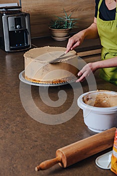 Unrecognisable woman decorating a delicious layered sponge cake with chocolate icing cream.