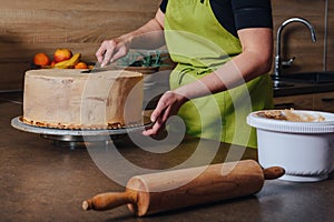 Unrecognisable woman decorating a delicious layered sponge cake with chocolate icing cream.