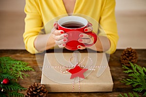Unrecognisable woman sitting at a table with beautifully wrapped christmas present, holding cup of tea. Gift wrapping concept.