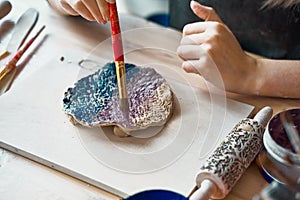 Unrecognised Woman making pattern on ceramic plate, hands close-up, focus on palms with paint brush. Creative hobby concept. Earn