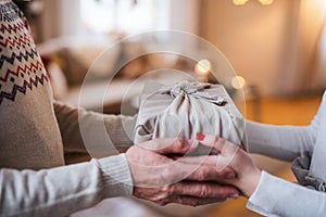 Unrecognizabe woman giving present to senior man indoors at home at Christmas.