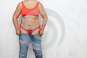 Unrecognizable adipose, fat, obese and overweight woman in red bikini pull and getting dressed in small size tight jeans