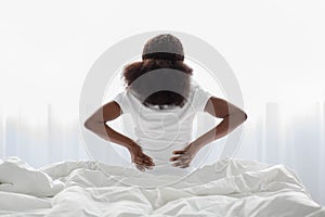 Unrecognizable african american woman sitting on bed, touching back