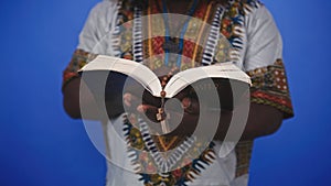 Unrecognizable African black man in traditional dress with rosary reading the Holy Bible
