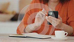 Unrecognizable African woman in orange blouse sits at table at home in office in cafe with cup of coffee holds mobile