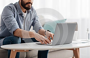 Unrecognizable bearded man working on pc, typing text or programming code on computer keyboard