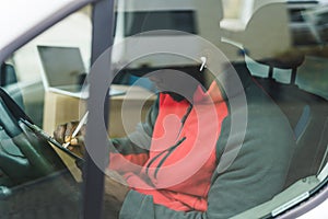 Unrecognizable Black adult man in black hat and red jacket working as a delivery person visible through the window of