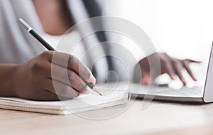 Unrecognizable female employee taking notes while working on laptop in office