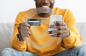 Unrecognizable black guy holding cellphone and credit card