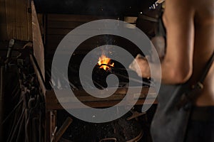 Unrecognizable blacksmith working with the furnace fire in his metal workshop