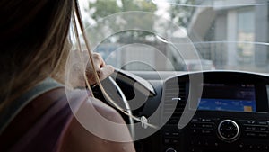 unrecognizable blonde woman driving car turn steering wheel and drives forward through city. girl holds her hand behind