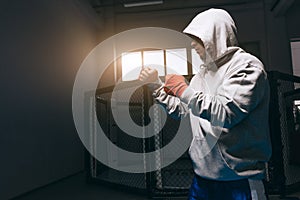 Unrecognizable boxer in grey hoodie with hood down over his eyes trains in gym.