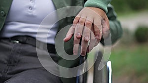 Unrecognizable boy holding hand of disabled girl on wheelchair armrest. Close-up palms of caring empathetic child and