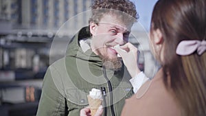 Unrecognizable brunette woman cleaning boyfriend`s nose dirty with ice cream. Positive young man smiling and looking at