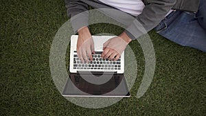 Unrecognizable businessman typing on his laptop lying on a lawn, top view