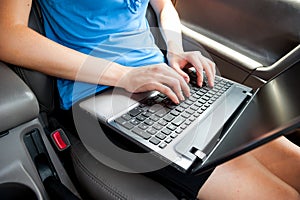 Unrecognizable businesswoman sitting in car with laptop computer on her knees