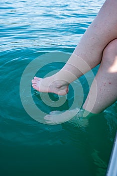 Unrecognizable caucasian woman dipping her bare feet in clean and clear lake water. Sunny summer day