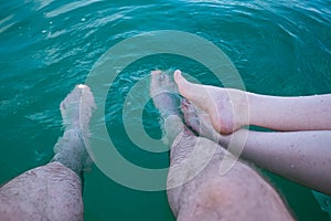 Unrecognizable caucasian woman and man dipping their bare feet in clean and clear lake water. Sunny summer day