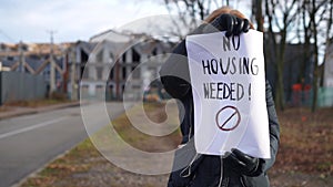 Unrecognizable Caucasian woman protesting with No housing needed banner outdoors. Slim protestor on autumn spring day