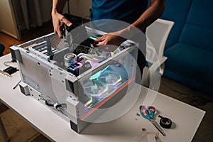 Unrecognizable computer technician installing new graphics card into modern custom-built pc with RGB lighting, enhancing