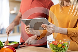 Unrecognizable couple cooking healthy dinner, checking recipes online