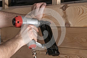 Unrecognizable cropped man hands using pneumatic stapler, nail gun for wooden board. Making layout on wooden plank. DIY