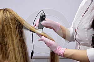 Unrecognizable doctor cosmetologist examines head skin of female patient with special dermatology equipment system