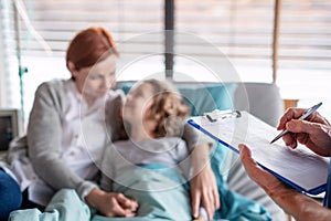 Unrecognizable doctor examining a small hospitalized girl with mother in hospital.