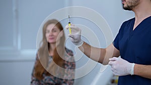 Unrecognizable doctor preparing syringe with facelift injection standing on the right with blurred woman waiting at