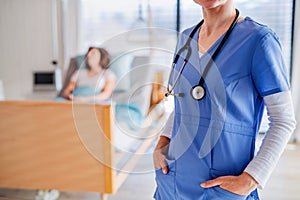 Unrecognizable doctor standing in hospital room, patient in the background.