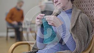 Unrecognizable elderly Caucasian woman knitting in armchair. Mature retiree spending free time in nursing home with