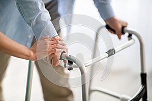 Unrecognizable elderly man using walker, young doctor supporting and helping him at retirement home