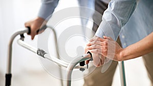 Unrecognizable elderly man using walker, young doctor supporting and helping him at retirement home