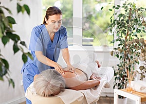 Unrecognizable elderly woman lies face down on couch and enjoy spa treatments, shoulder massage