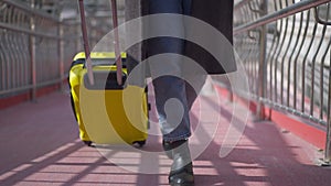 Unrecognizable elegant young slim woman walking with yellow travel bag in slow motion on sunny day outdoors. Caucasian