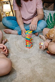 Unrecognizable family having fun making a tower with wooden stacking piece game over carpet at home