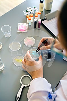 Unrecognizable female chemist examining blue glitter in facial cream sample on laboratory