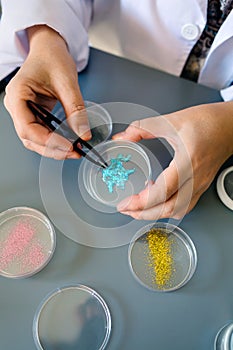 Unrecognizable female chemist technician examining a blue glitter sample over petri dish on lab