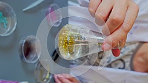 Unrecognizable female chemist technician hand shaking flask with golden glitter sample on lab