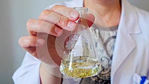 Unrecognizable female chemist technician hand shaking flask with golden glitter sample on lab