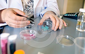 Unrecognizable female chemist technician holding a blue glitter sample over petri dish on lab