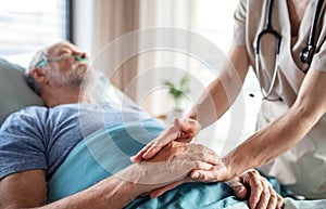 Unrecognizable female doctor examining senior man in bed in hospital.