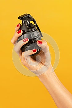 Unrecognizable female hand holding black grenade against yellow backdrop