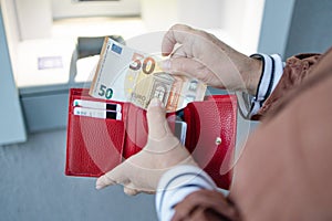 Unrecognizable female holding in hands wallet with euro money near the ATM. Withdrawing cash to pay for services, a loan