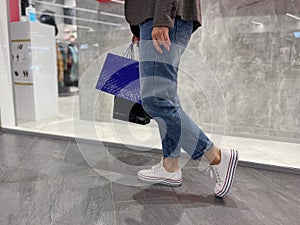 Unrecognizable female holds in hand shopping bags walking in the shopping mall. Close up of women legs in shopping