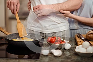 Unrecognizable female and male fry together eggs and make tomatoes salad, stand on kitchen, prepare breakfast involved