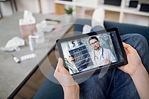 Unrecognizable female patient having video chat with male doctor on digital tablet at home, getting online consultation